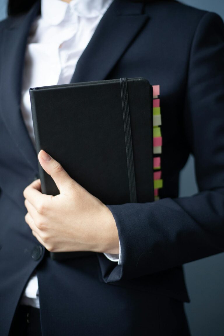 A businesswoman in a suit holds a planner with colorful tabs in an office setting.