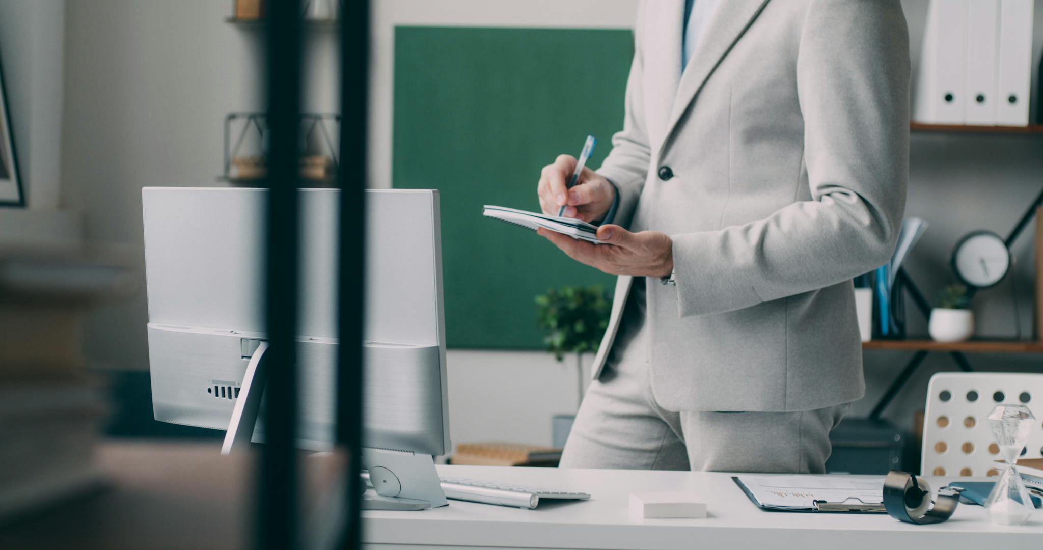 A focused businessman in a modern office, taking notes in front of a computer.