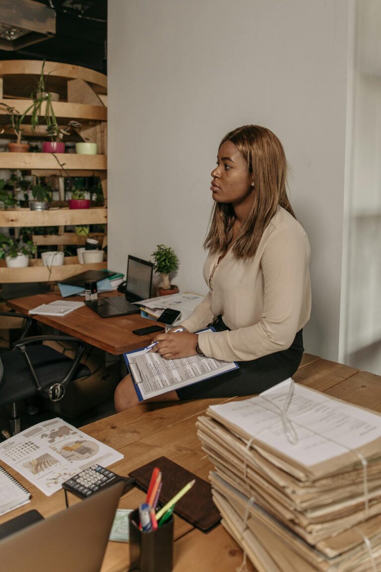 A young, professional woman reviewing documents at a desk in an indoor office setting.