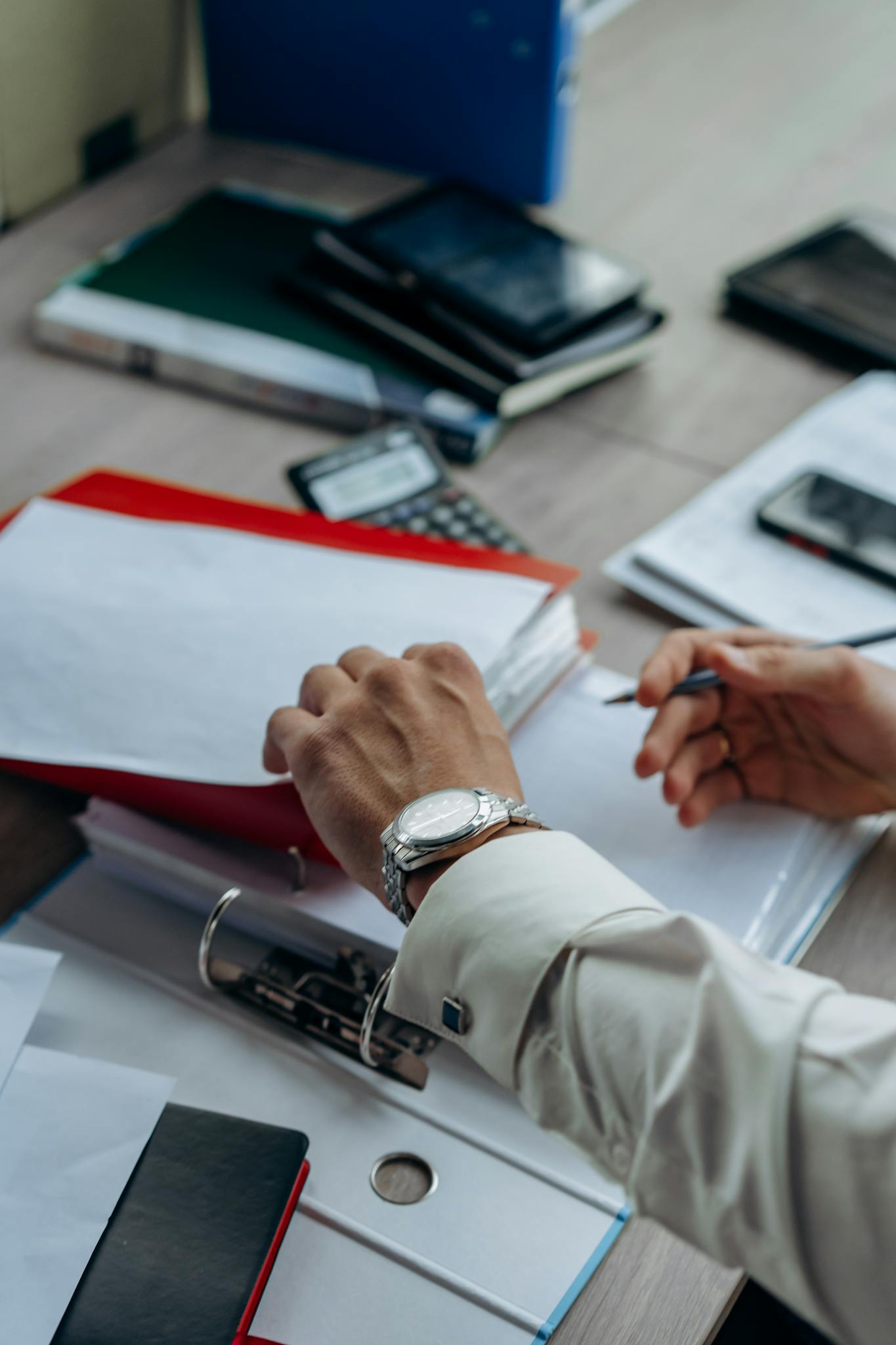 Businessman's hands organizing paperwork and files on a busy office desk.