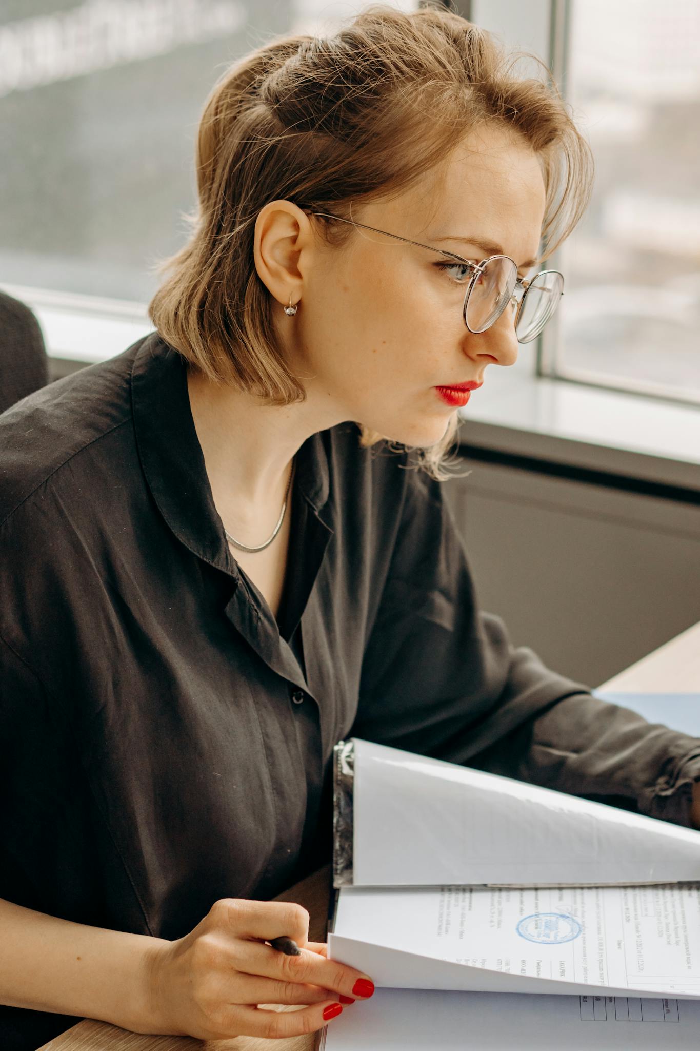 Serious woman with eyeglasses working on paperwork in an office setting.
