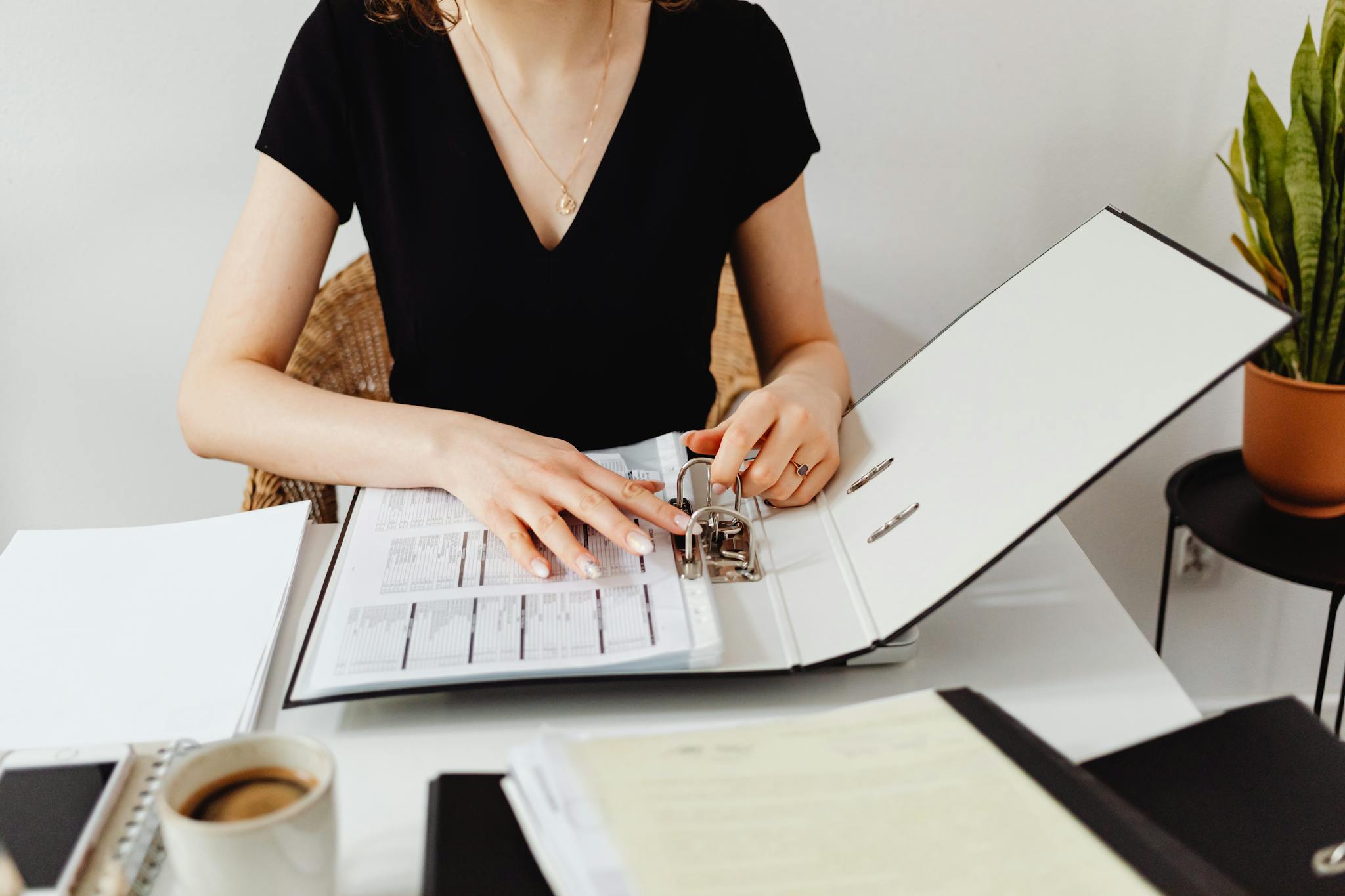 Woman organizing documents in a binder at a stylish office desk with coffee.